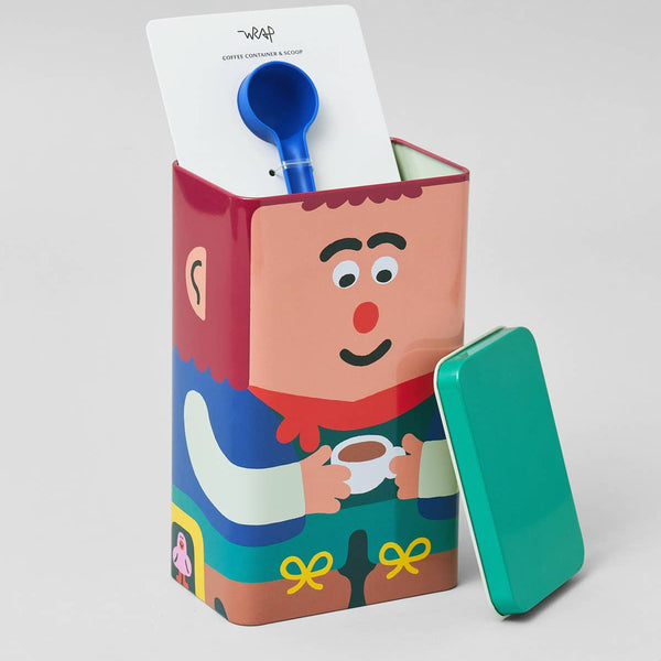 Colorful tin box with cartoon character design, blue spoon, and white paper on a light gray background