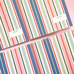 Two notebooks with colorful striped design and 'NOTES' label on a matching pink background.
