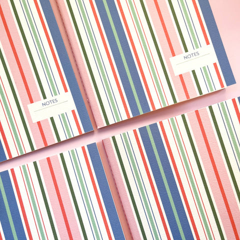 Two notebooks with colorful striped design and 'NOTES' label on a matching pink background.