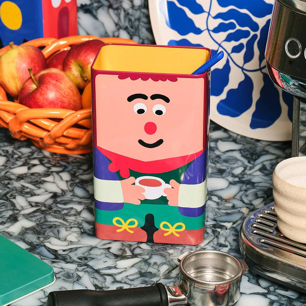 Cartoon character tea box on a marble surface with coffee-making items.