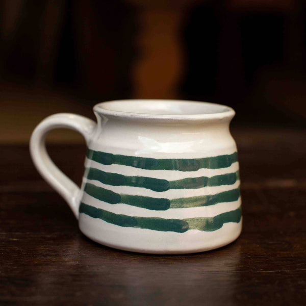 Ceramic mug with green stripes on a dark wooden surface