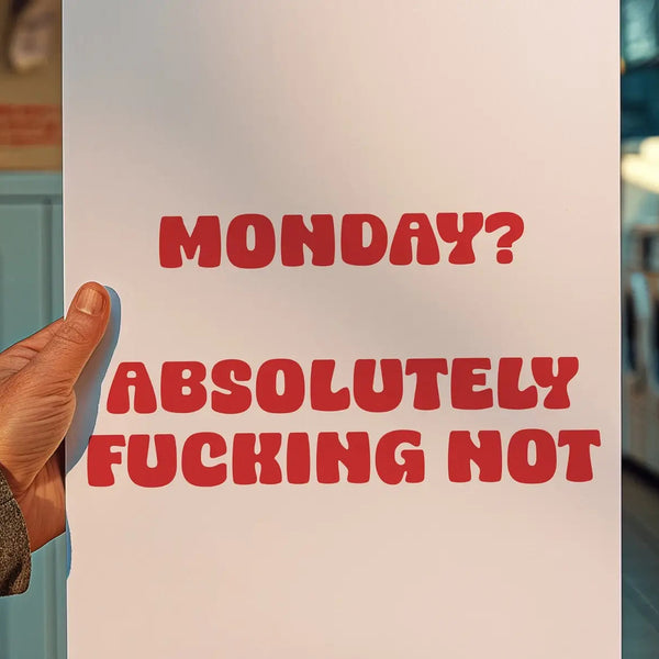 Hand holding a sign with red text 'MONDAY? ABSOLUTELY FUCKING HOT' in a laundromat.