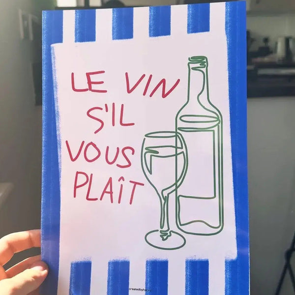Hand holding a sign with 'Le Vin S'il Vous Plait' text and wine graphics in a kitchen setting.