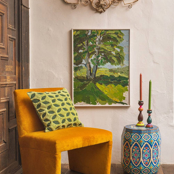 Yellow chair with a green pillow, framed artwork, and decorative vase in a room.