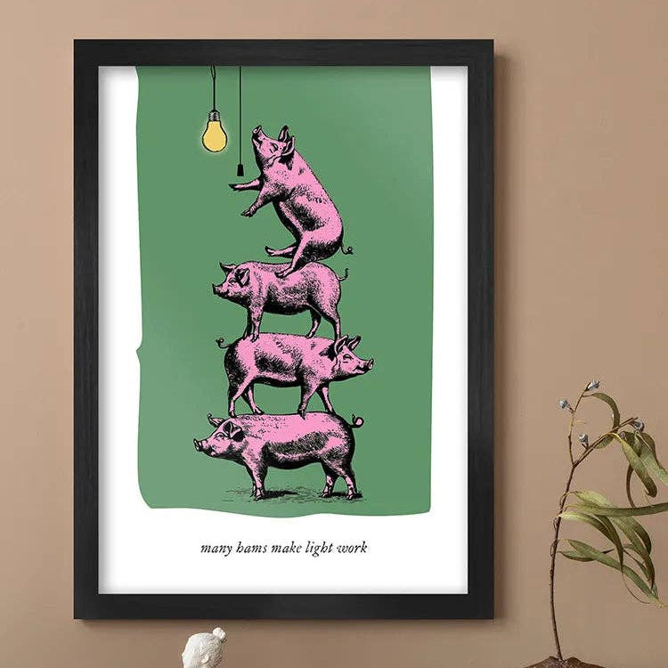 Framed artwork with pink pigs and a light bulb on a green background, displayed on a wall.