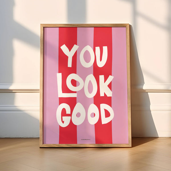 Framed poster with 'YOU LOOK GOOD' text on a pink and red striped background, placed against a white wall.