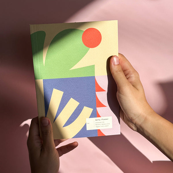 Colorful geometric design book held by a hand on a pink background