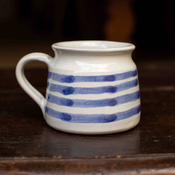 White ceramic mug with blue stripes on a dark wooden surface