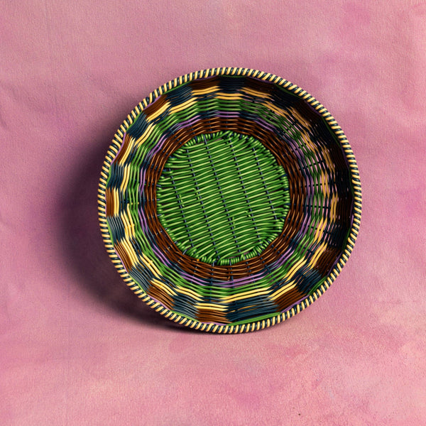 Decorative woven basket with a green center on a pink background