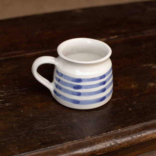 Small white mug with blue stripes on a dark wooden surface